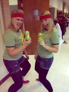 two women in green shirts and black pants holding cans of canned drink with red headbands