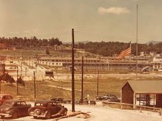 an old photo of cars parked on the side of a road in front of buildings