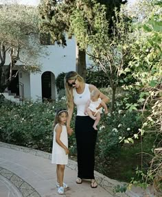 a woman and two children are standing on the sidewalk in front of some bushes with flowers