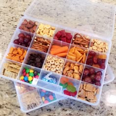 a plastic container filled with lots of different types of snacks and candies on top of a marble counter