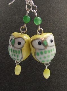 two yellow owls with green beads are hanging from silver earwires on a black surface