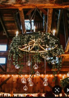 a chandelier hanging from the ceiling in a barn with lights and greenery