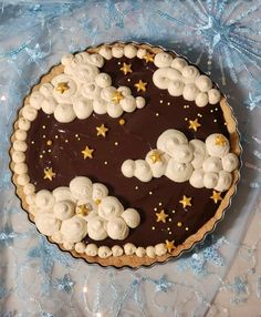 a chocolate tart decorated with stars and clouds on a blue tableclothed surface