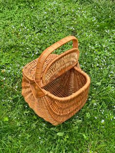 an empty wicker basket sitting on the grass in front of some wildflowers