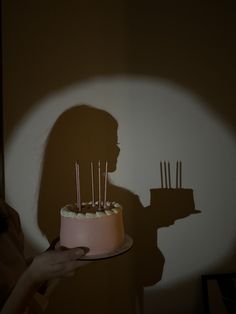 the shadow of a person holding a cake with candles on it in front of a wall