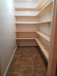 an empty walk in closet with shelves and tile flooring