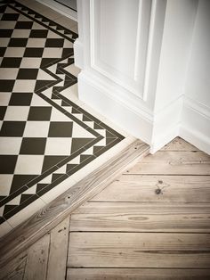 a black and white checkerboard floor next to a wall with an open door