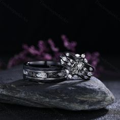 two wedding rings sitting on top of a rock next to purple flower petals in the dark