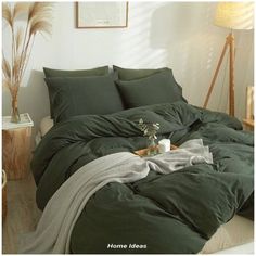 a bed with green sheets and pillows in a room next to a plant on the floor