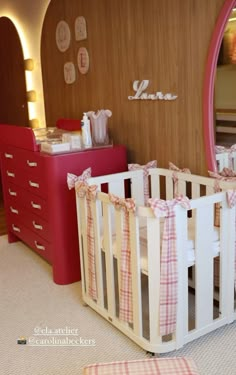 a baby's crib in front of a mirror and dresser with pink drawers