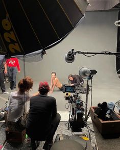 three people sitting in front of a camera on a tripod and another person standing behind them