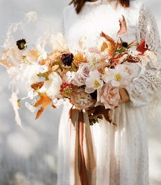 a woman holding a bouquet of flowers in her hands and wearing a white lace dress