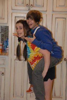 a boy and girl are standing in front of the kitchen cabinets with their arms around each other