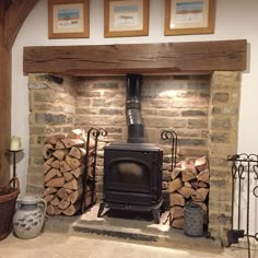 a wood burning stove in a stone fireplace with logs stacked on the hearth and framed pictures above it