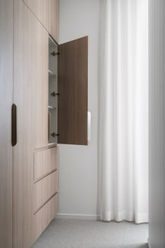 an open closet door in a white room with wooden cabinets and curtains on the window sill