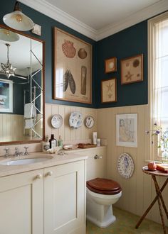 a bathroom with blue walls and pictures on the wall above the toilet, along with a wooden seat