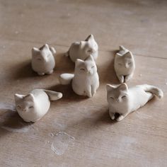 small white ceramic cats sitting on top of a wooden table next to another cat figurine