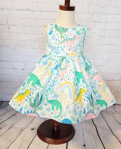 Display dress is a size 3t on a size 3t mannequin. It is shown with tulle petticoat which is NOT INCLUDED in the purchase of this dress. It is for display purposes only. This little pastel dinosaur dress features multi colored dinosaurs in a tropical jungle setting on a cream colored background . It would be perfect for a dinosaur themed birthday party or for any little one that loves dinos! The bodice is lined with soft cotton and it snaps in the back with Kam snaps for easy on and off. There a Summer Princess Dress With Ruffles For Playtime, Playful Summer Princess Dress For Dress-up, Spring Princess Dress With Ruffles For Playtime, Playful Sleeveless Princess Dress For Summer, Playful Sleeveless Summer Princess Dress, Cute Green A-line Dress, Whimsical Princess Dress For Dress-up In Summer, Playful Princess Dress For Spring Playtime, Cute A-line Dress For Dress-up Occasions