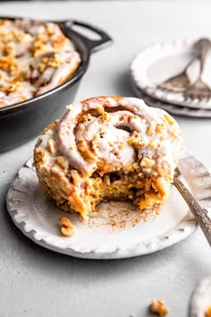 a cinnamon roll sitting on top of a white plate next to a fork and bowl