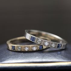 two diamond and sapphire wedding bands on top of a black leather case with gold trim