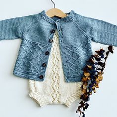 a baby's blue sweater and white bodysuit with flowers on the floor next to it