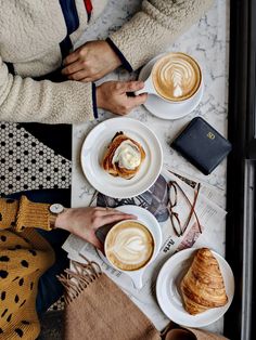 two people sitting at a table with coffee and croissants