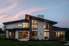 a modern house with large windows and grass in the front yard at dusk, lit up by lights