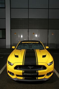 a yellow sports car parked in a parking lot at night with its hood up and stripes down