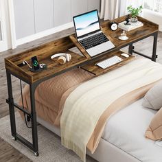 a laptop computer sitting on top of a wooden desk next to a bed with pillows