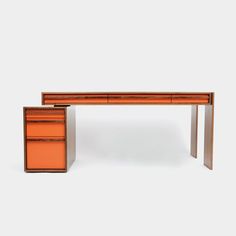 an orange desk sitting on top of a white floor next to a wooden cabinet with drawers