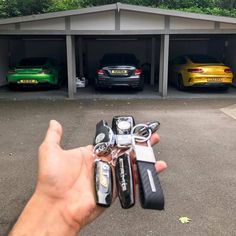 a hand is holding keys in front of three parked cars and two garages with their doors open