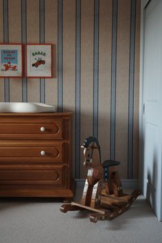 a wooden rocking horse next to a dresser with striped wallpaper and two pictures on the wall