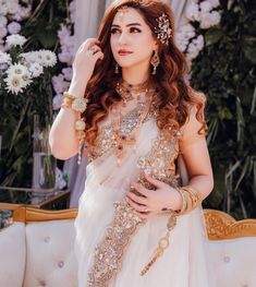 a woman in a white sari with gold jewelry on her neck and hands near her face