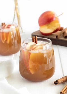 two glasses filled with apple cider and cinnamon sticks