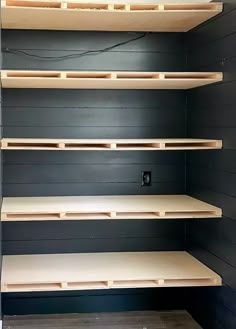 empty shelves in a room with black walls and wood flooring on the sides,