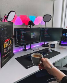 a person holding a cup of coffee in front of three computer monitors