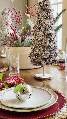 a christmas table setting with red and white plates, napkins, silverware and a pine cone centerpiece