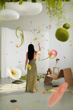 a woman standing in front of a wall with flowers and plants hanging from the ceiling