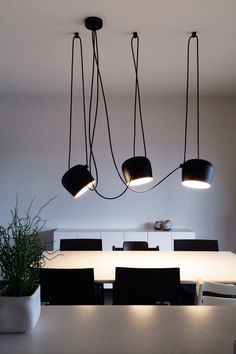 three lights hanging from the ceiling above a dining room table with black chairs and white walls