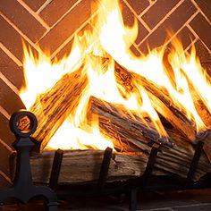 a fire burning inside of a fireplace next to a brick wall and wooden logs in front of it