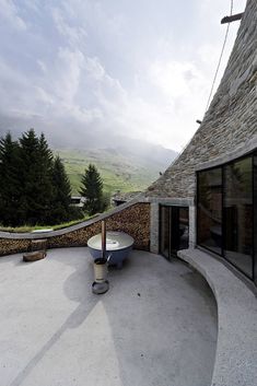 an unusual house in the mountains with a circular patio and stone walls, overlooking trees and rolling hills