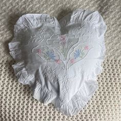 a white heart shaped pillow sitting on top of a bed covered in ruffled material