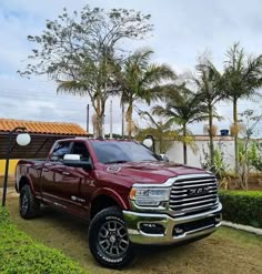 a red ram truck parked in front of a house with palm trees and shrubs around it