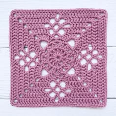 a pink crocheted square on top of a white wooden surface with an openwork design