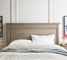 a bed with white linens and pillows in a small room next to a painting on the wall