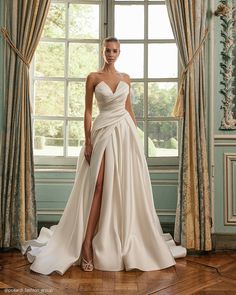 a woman standing in front of a window wearing a wedding dress with high slits