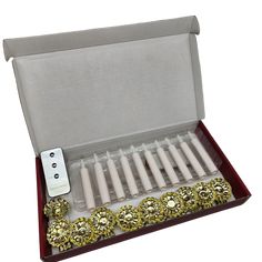 an open box with several white candles and some gold decorations in it's lid