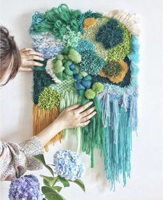 a woman is working on a piece of art made from yarn and felt with flowers in the foreground