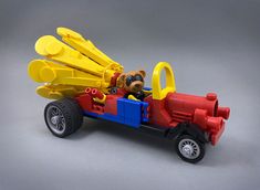 a toy bear is in the back of a red and blue truck with yellow wheels