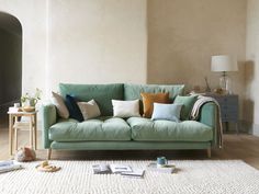 a living room with a green couch and various pillows on the floor next to a white rug